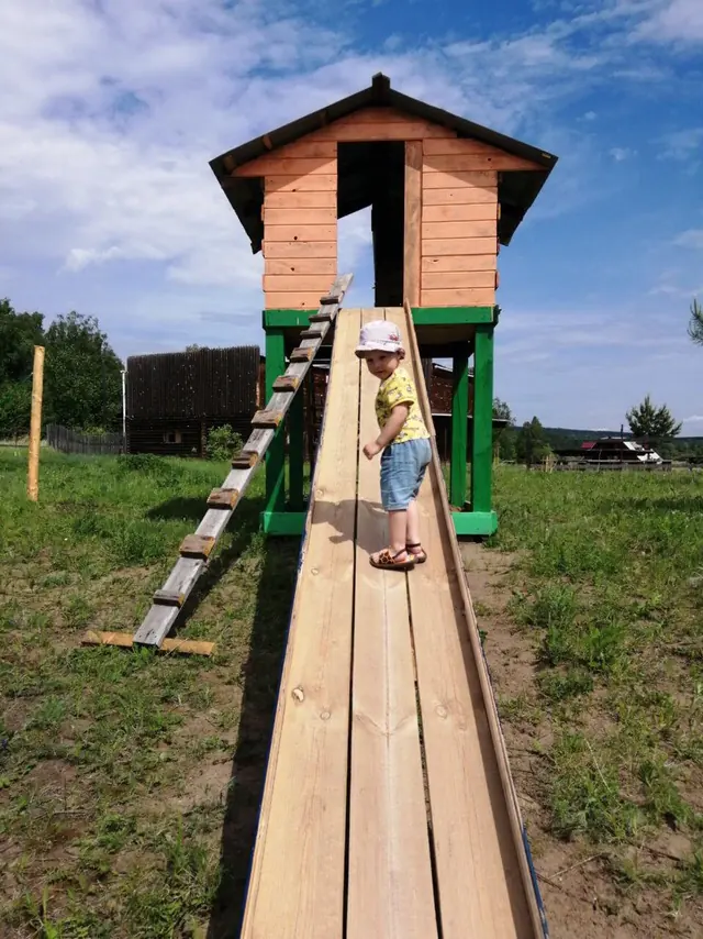 Ребёнок на деревянной горке у игрового домика